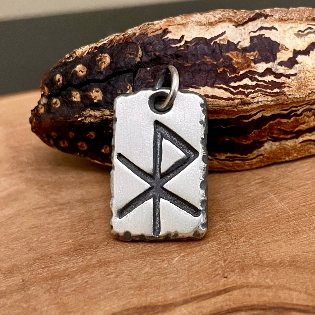Silver pendant with a viking rune symbol on a wooden surface