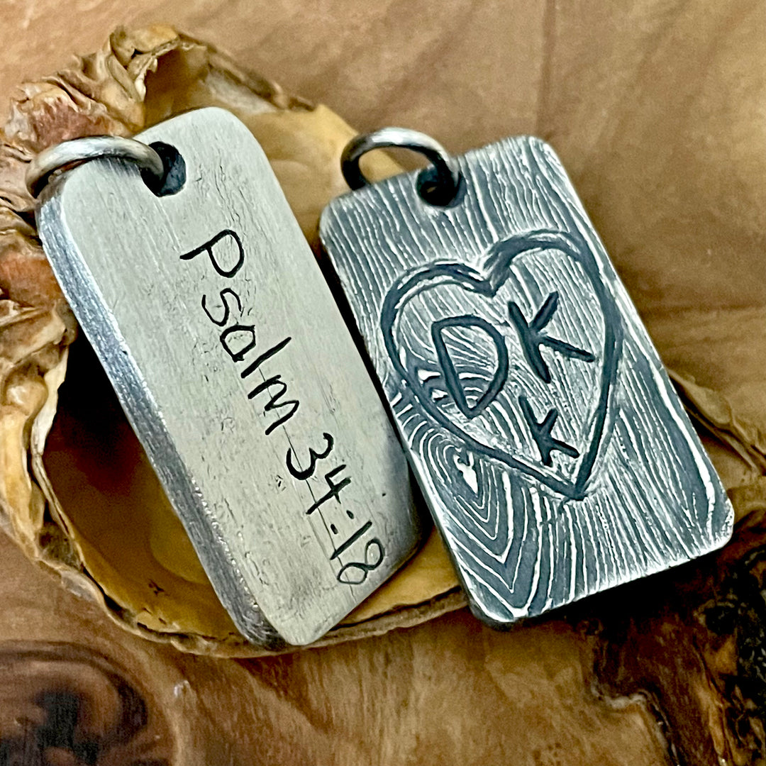 oxidized sterling silver pendant tag with textured tree bark back ground and hand carved heart with personalized initials on wood display