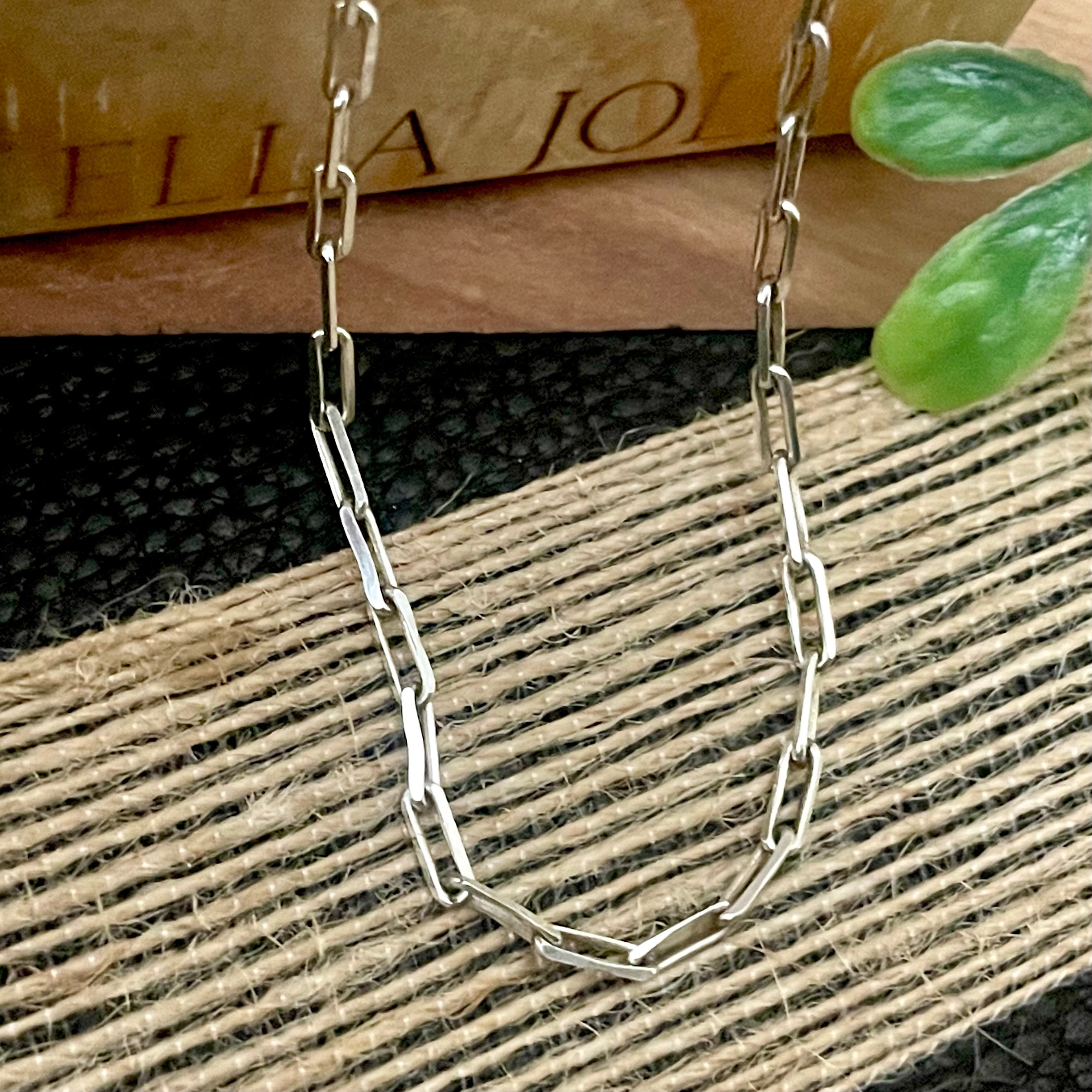 Silver chain necklace on a textured surface with a plant in the background