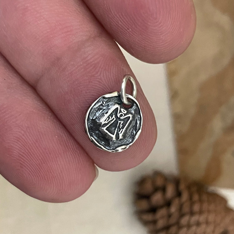 Silver guardian angel pendant held between fingers with a blurred background