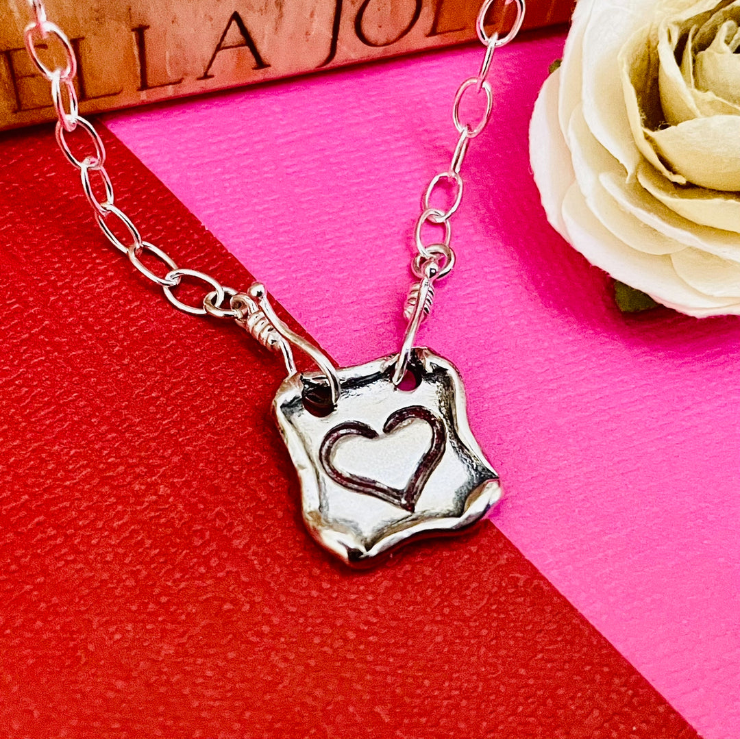 Square-shaped artisan made sterling silver heart necklace on pink and red background 