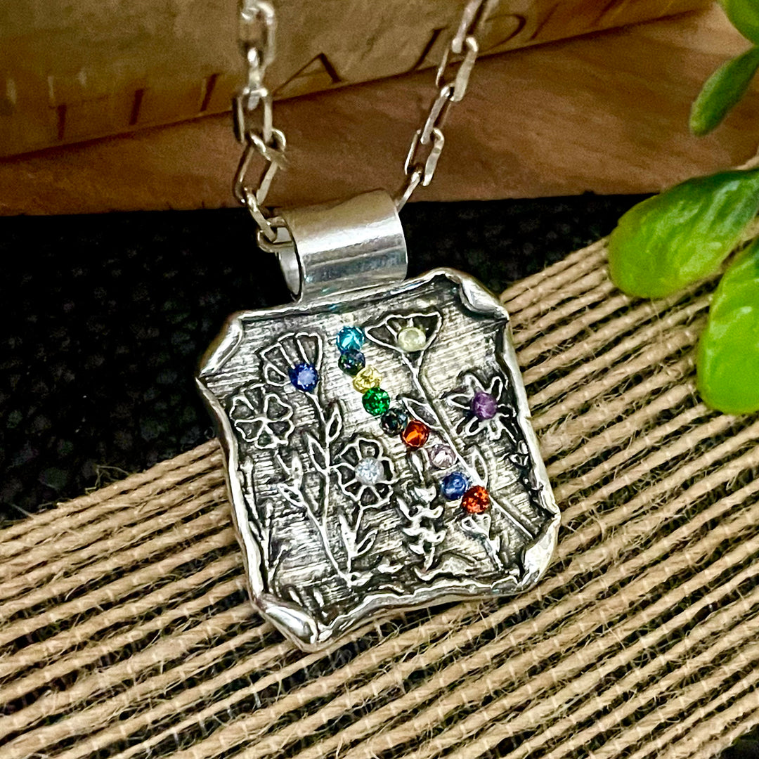 Sterling Silver necklace with a decorative flower garden design pendant featuring colorful birthstones on a textured surface.