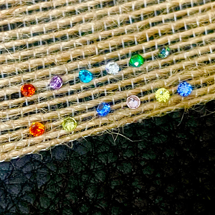 All 12 months close-up of colorful crystal cz rhinestone birthstones on beige fabric with a dark background