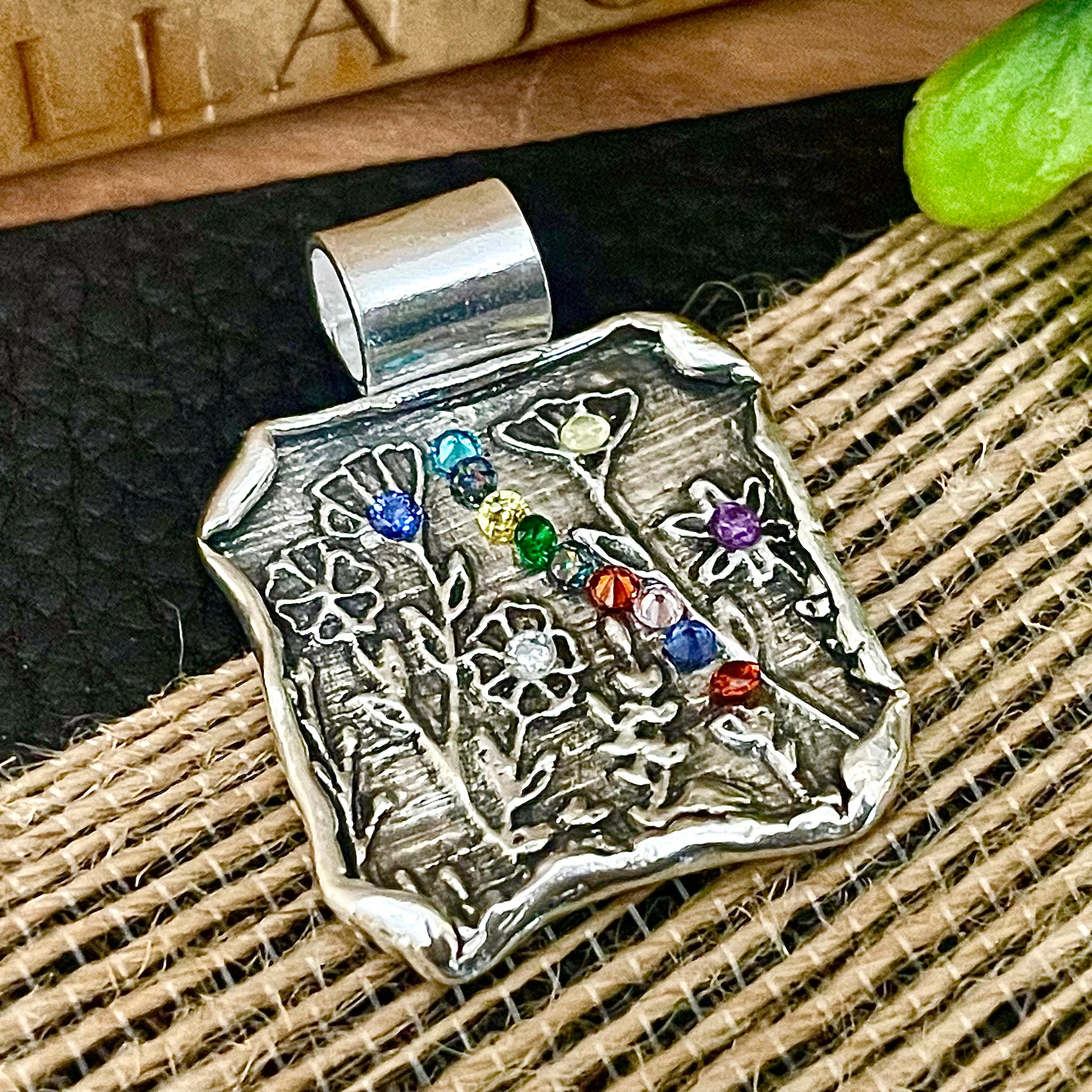 Silver pendant with colorful custom birthstone gemstones on a textured surface