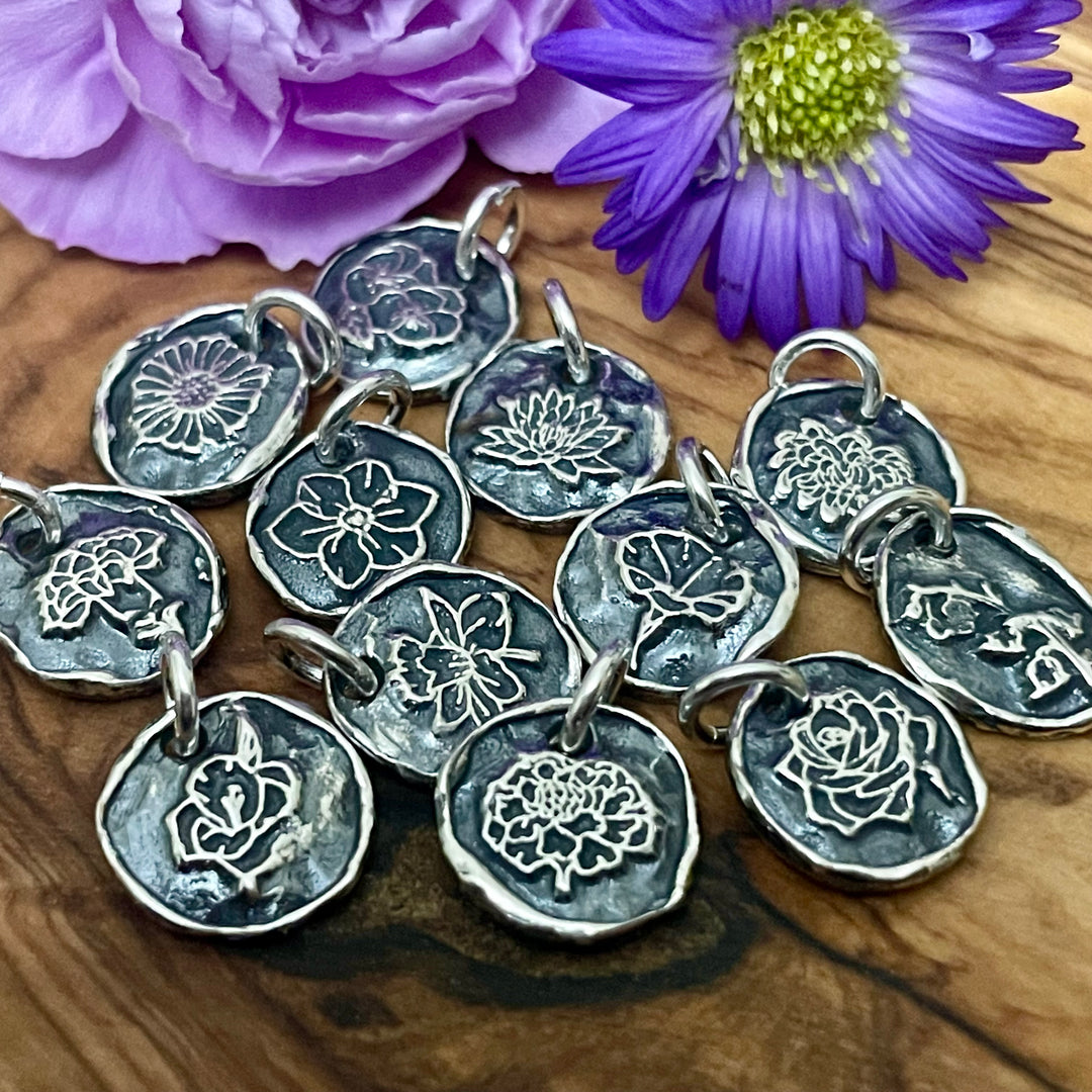Sterling silver floral charms on a wooden surface with purple flowers.
