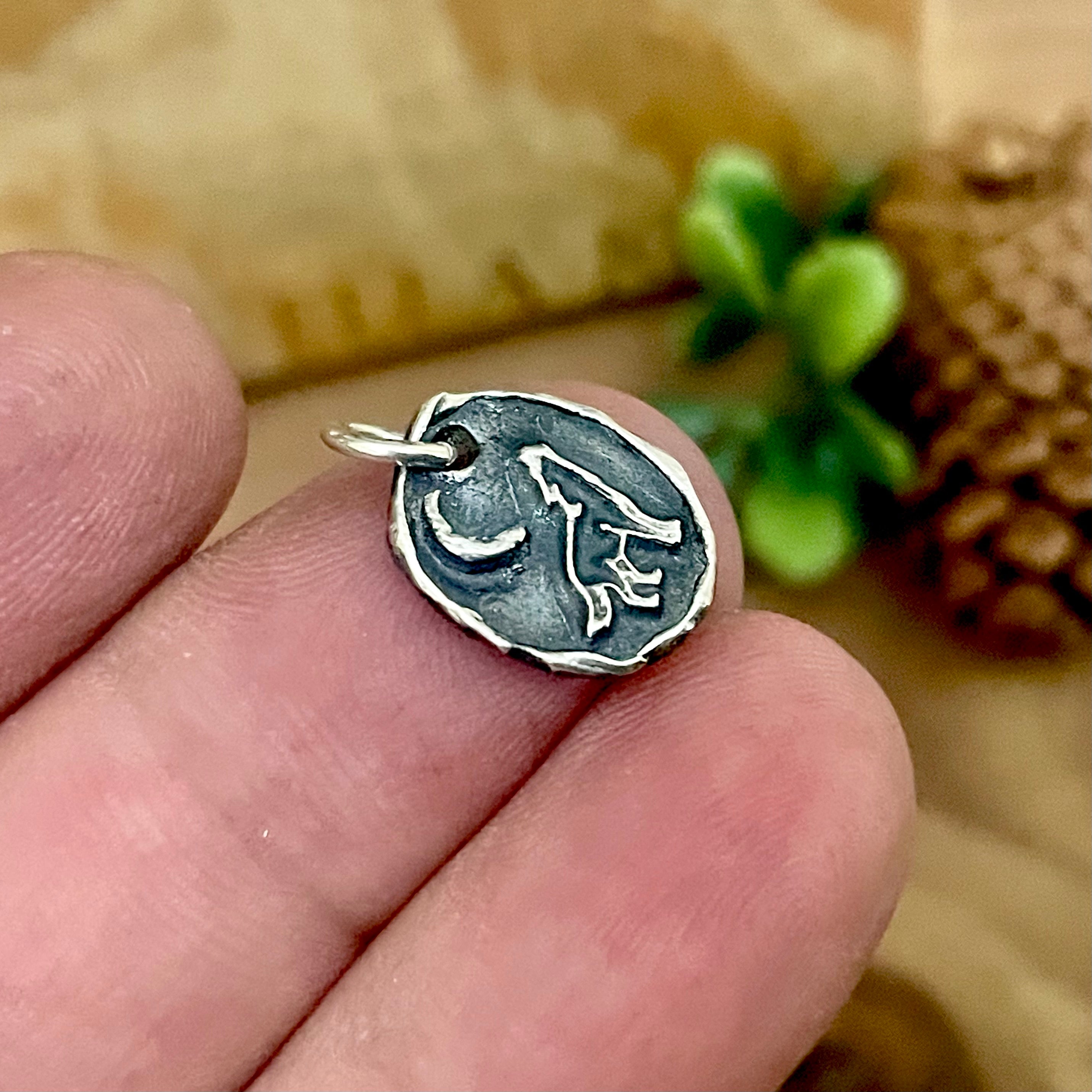 Sterling Silver pendant charm with a coyote howling at the moon held between fingers with a blurred background