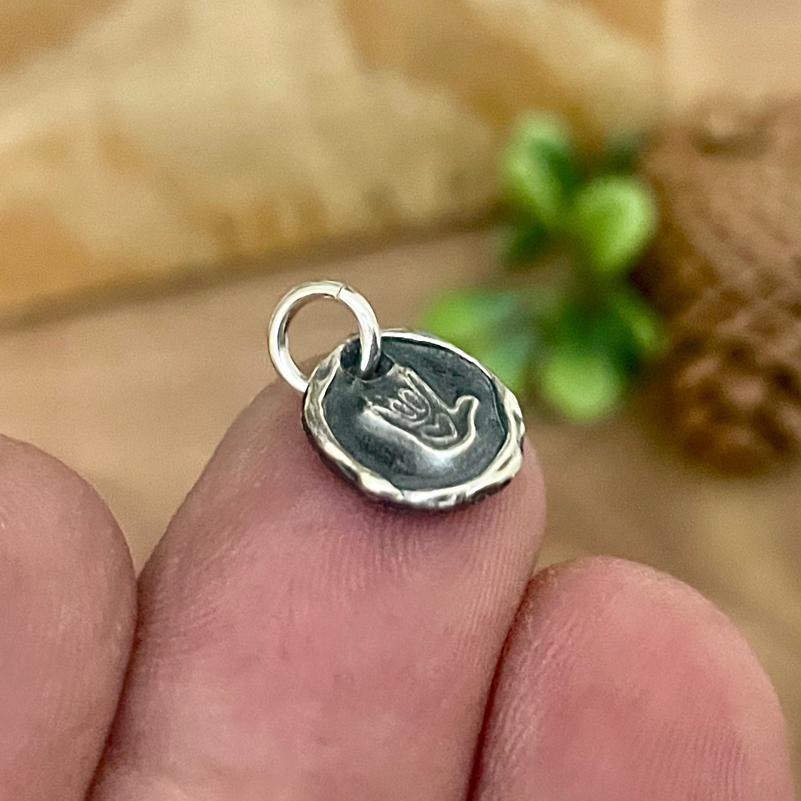 Silver I love you hand sign pendant held between fingers with a blurred natural background