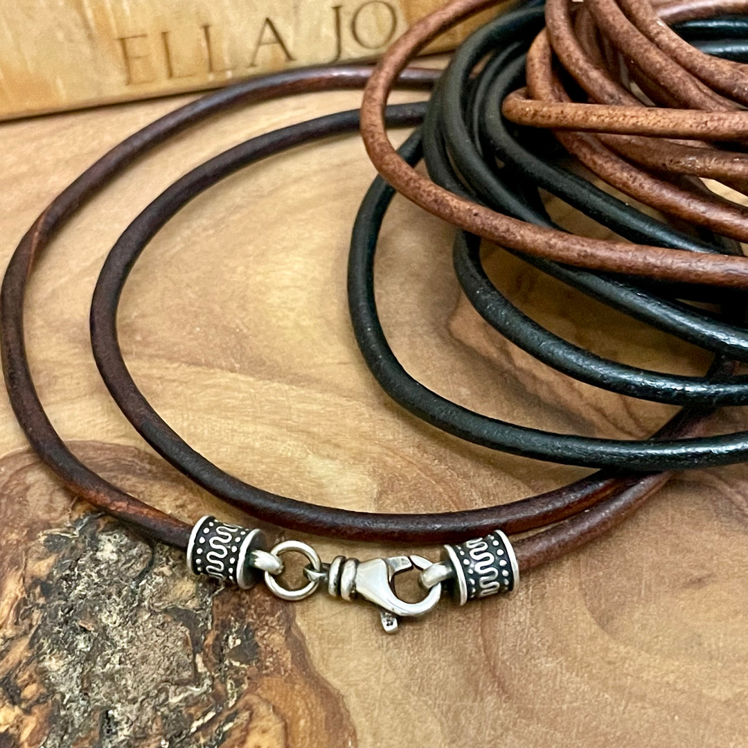 Brown and black leather cord necklace with silver clasp on a wooden surface