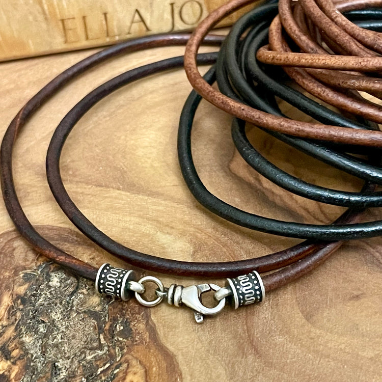 Brown and black leather cord necklace with silver clasp on a wooden surface