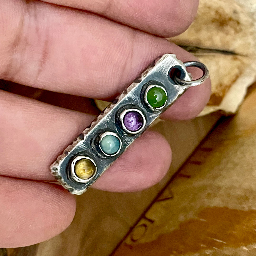 Silver bar pendant with four custom birthstones held by a hand against a wooden background