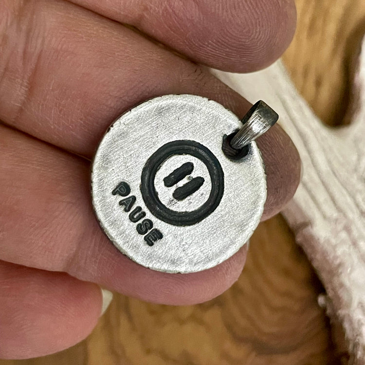 Round sterling silver back side of a yin yang pendant with the word and symbol of Pause. Sterling silver Bail shown in hand. Handforged and carved by Ella Joli