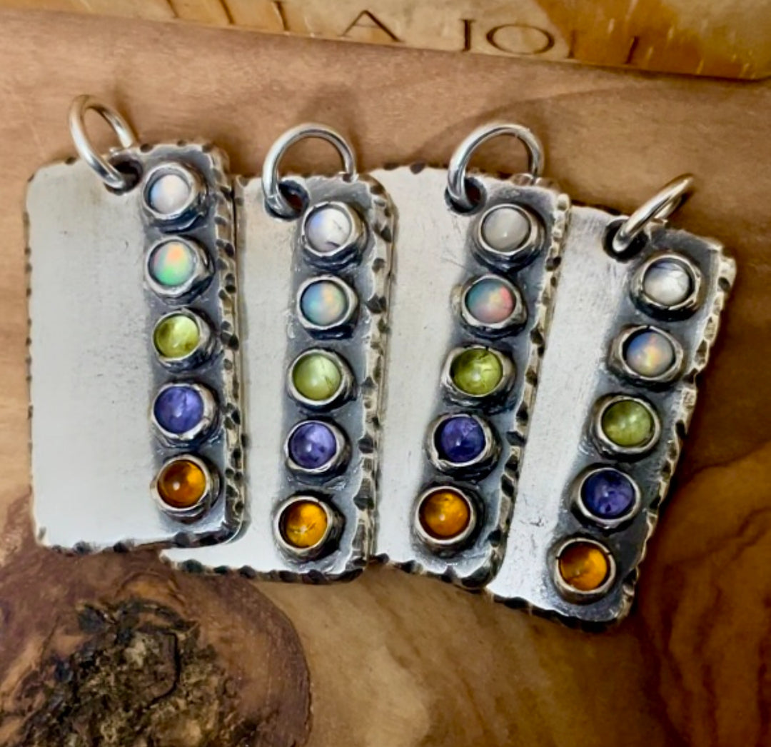 Four sterling silver ectangle shaped pendants with five custom family birthstones on each pendant. Displayed on wood background. 