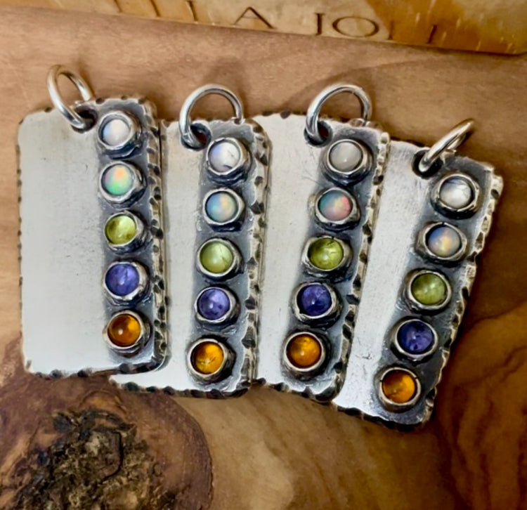 Four sterling silver ectangle shaped pendants with five custom family birthstones on each pendant. Displayed on wood background. 