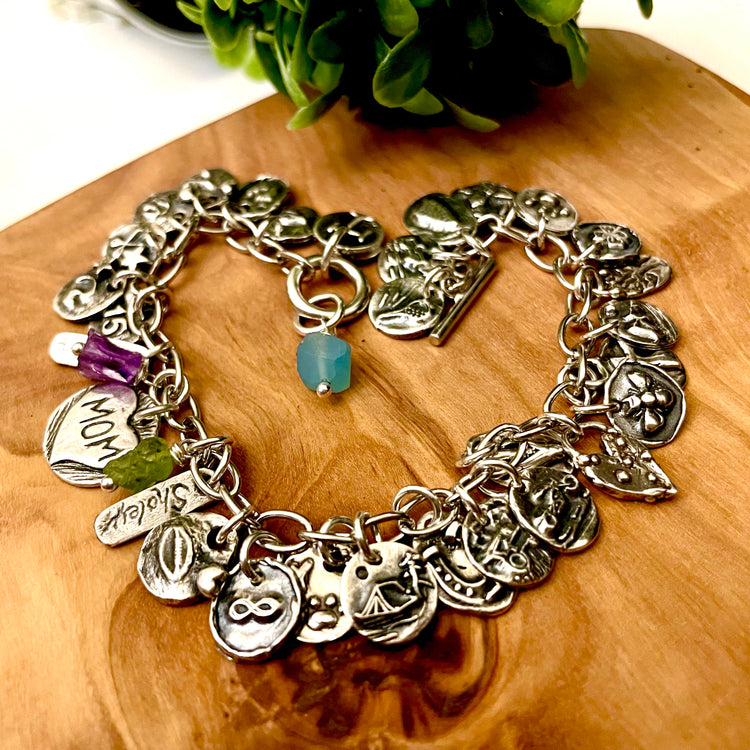 Silver charm bracelet on a wooden surface with a plant in the background