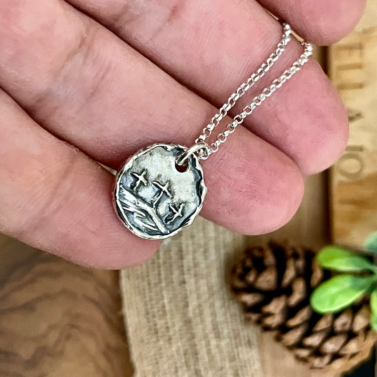 sterling silver three crosses of calvary necklace, handmade christian charm pendant, personalized cross necklace engraving,baptism gift. A sterling silver necklace with a round pendant held by a hand, wooden background with pine cone.