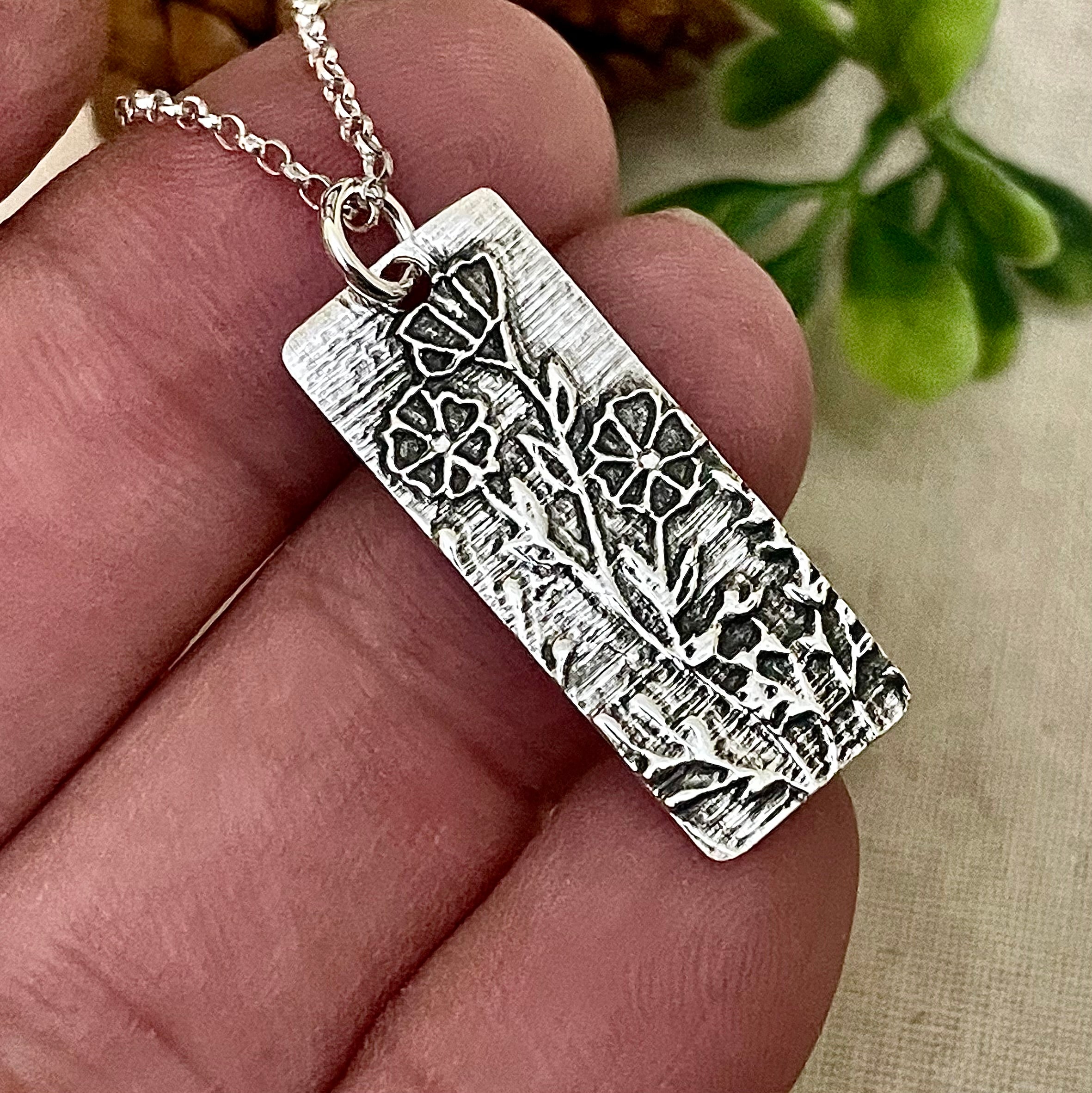Silver textured pendant with flowers held in a hand with a natural background