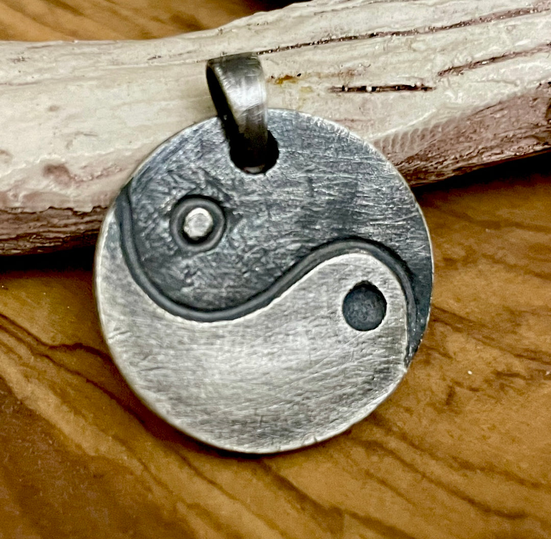 Round custom sterling silver artwork pendant oxidized with bail shown on wood background. This pendant is shown carved with yin yang design for men. oxidized sterling silver. Hand forged by lla Joli