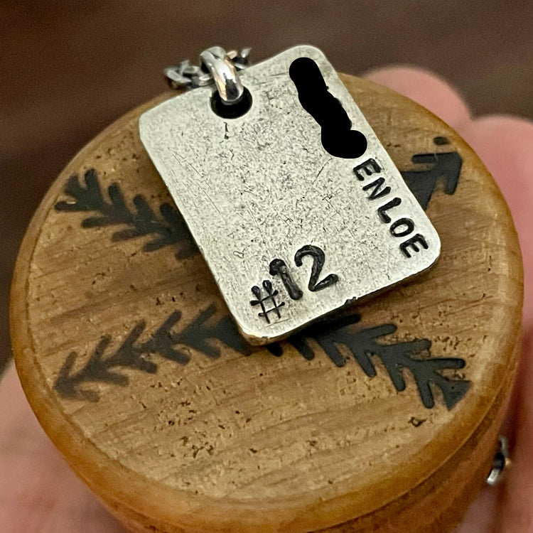 Sterling silver rectangle shaped pendant with custom engraved name and baseball number. Sitting on wood background.