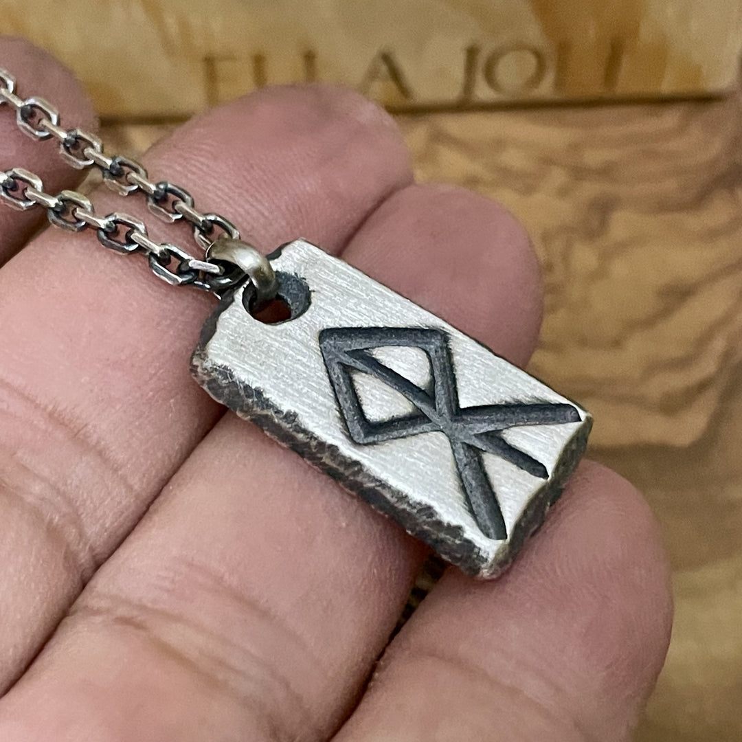 Silver pendant with a geometric courage rune design held in a hand against a wooden background