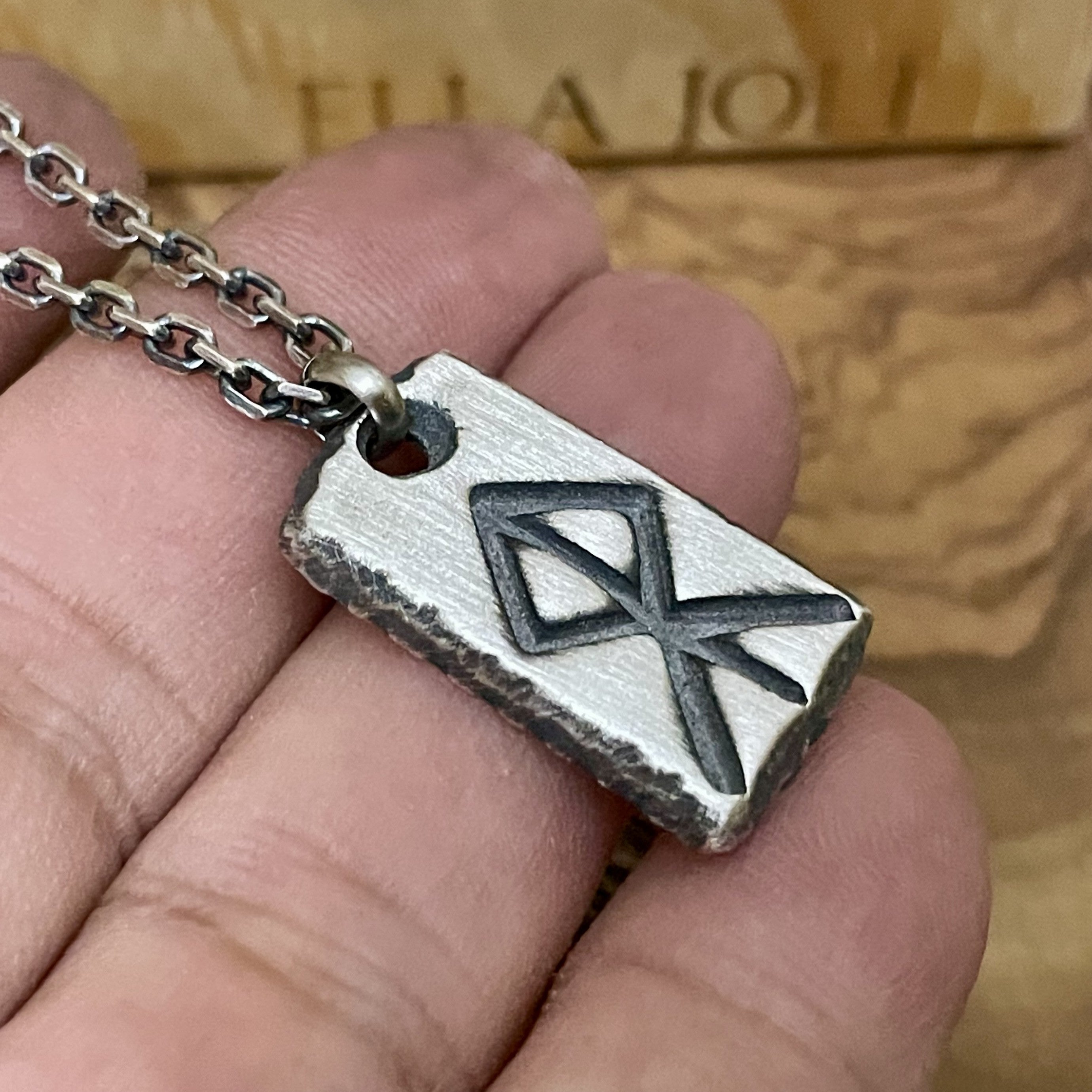 Silver pendant with a geometric courage rune design held in a hand against a wooden background