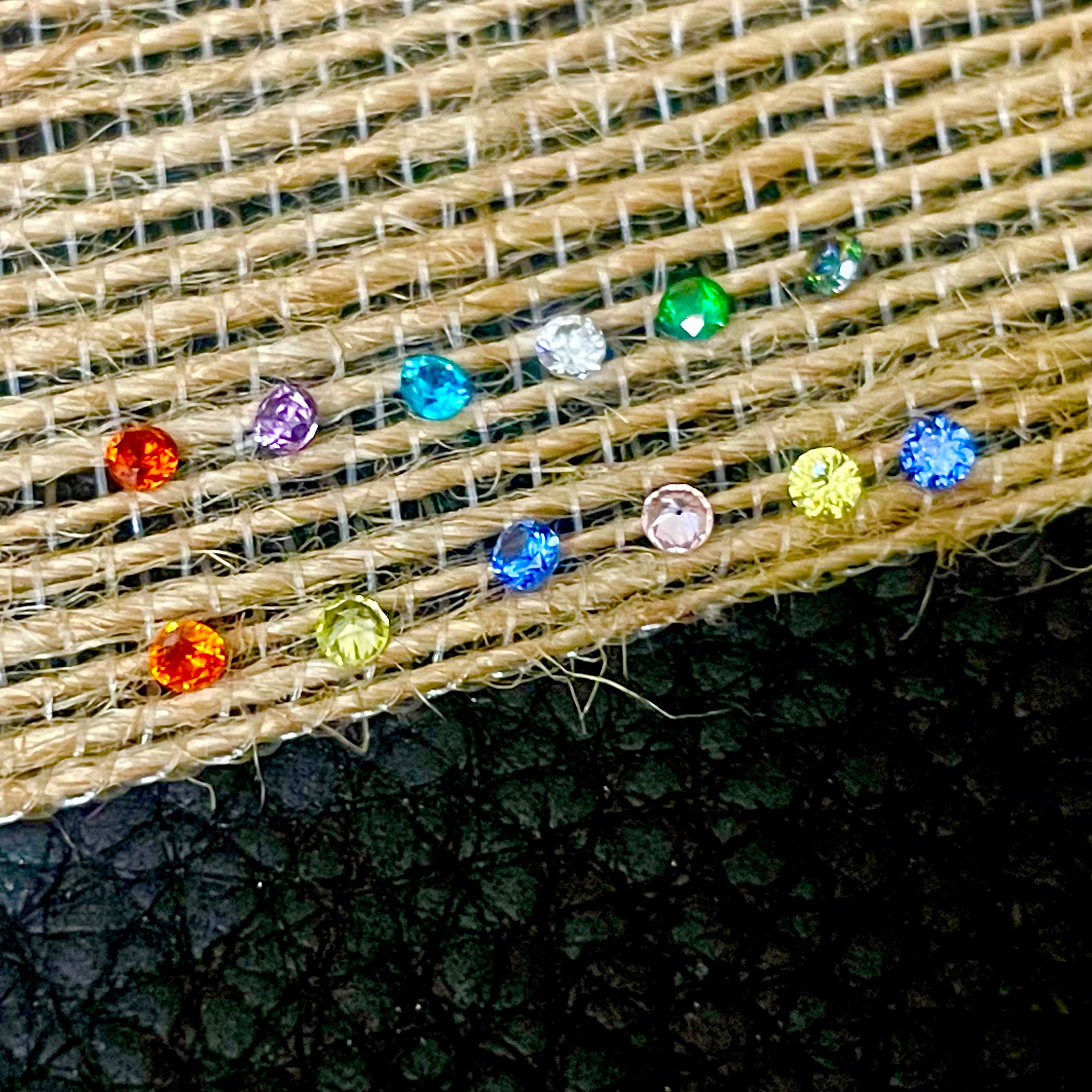 Close-up of colorful crystal  rhinestone birthstones on beige fabric with a dark background