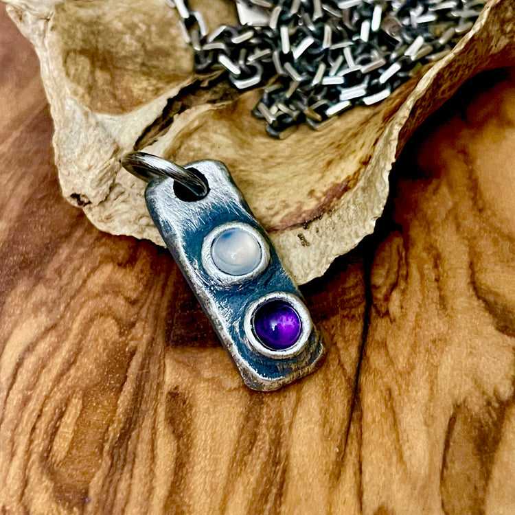 two stone gemstone bar pendant one inch tall with 4mm round natural stones shown in amethyst and moonstone. Masculine with oxidized finish. Displayed on wood background