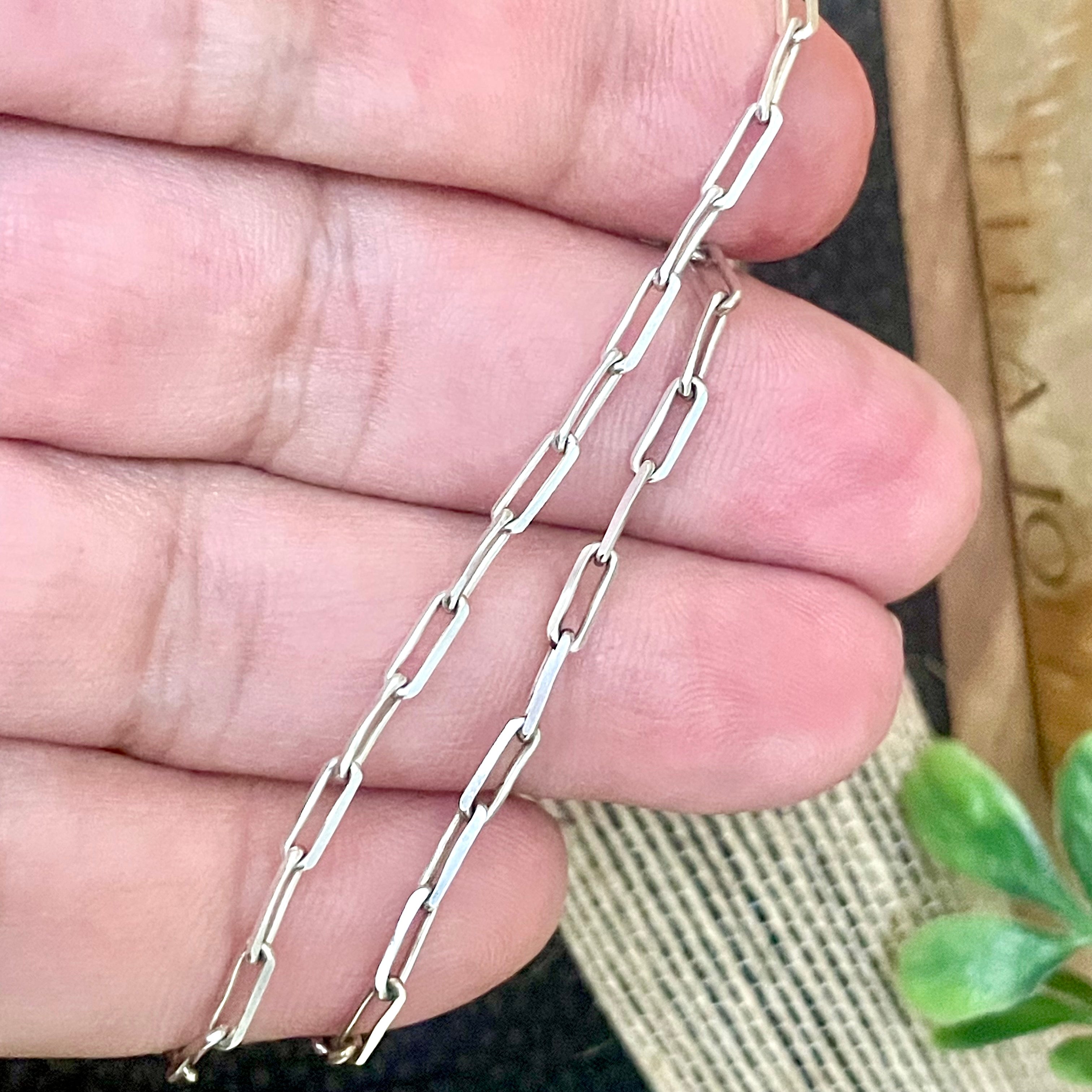 Silver dainty rectangle link chain held between fingers with a blurred background