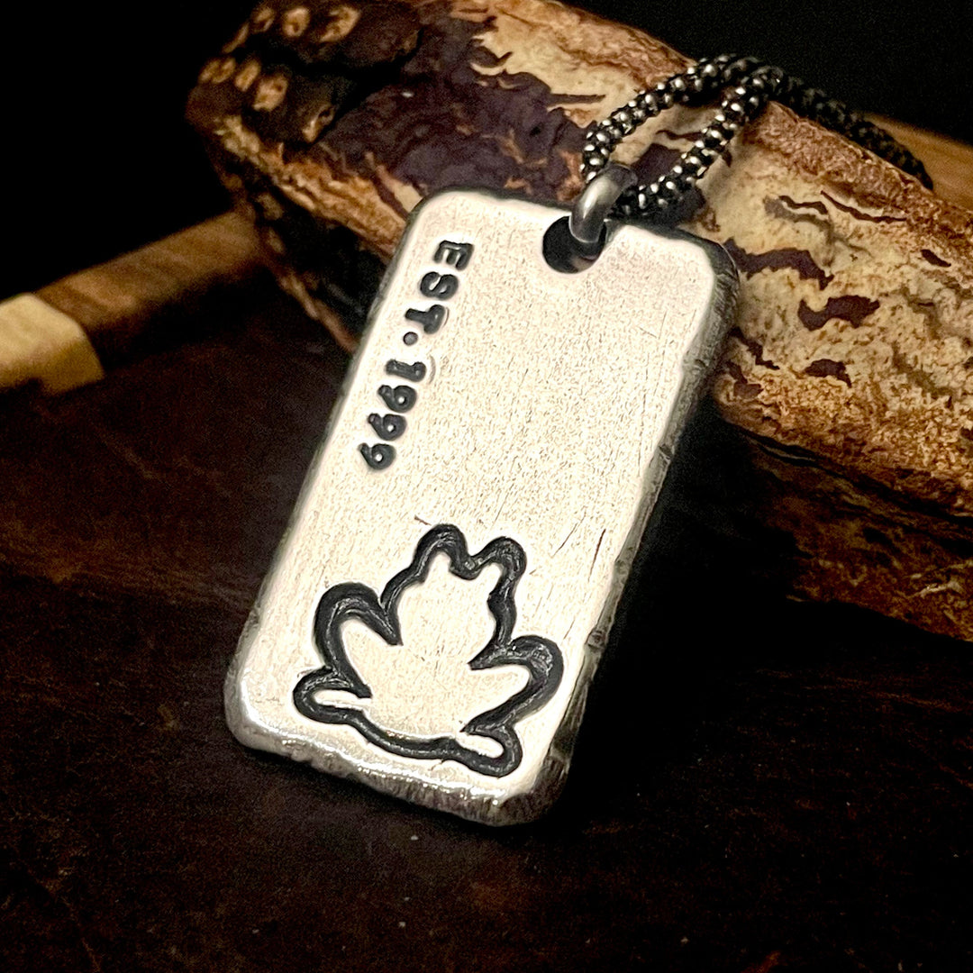 custom logo pendant with custom engraved established date of 1999 and a frog image in bottom right corner. all personalized with your artwork and dates on rectangle sterling silver pendant. Shown with sterling silver chain on wood background by Ella Joli