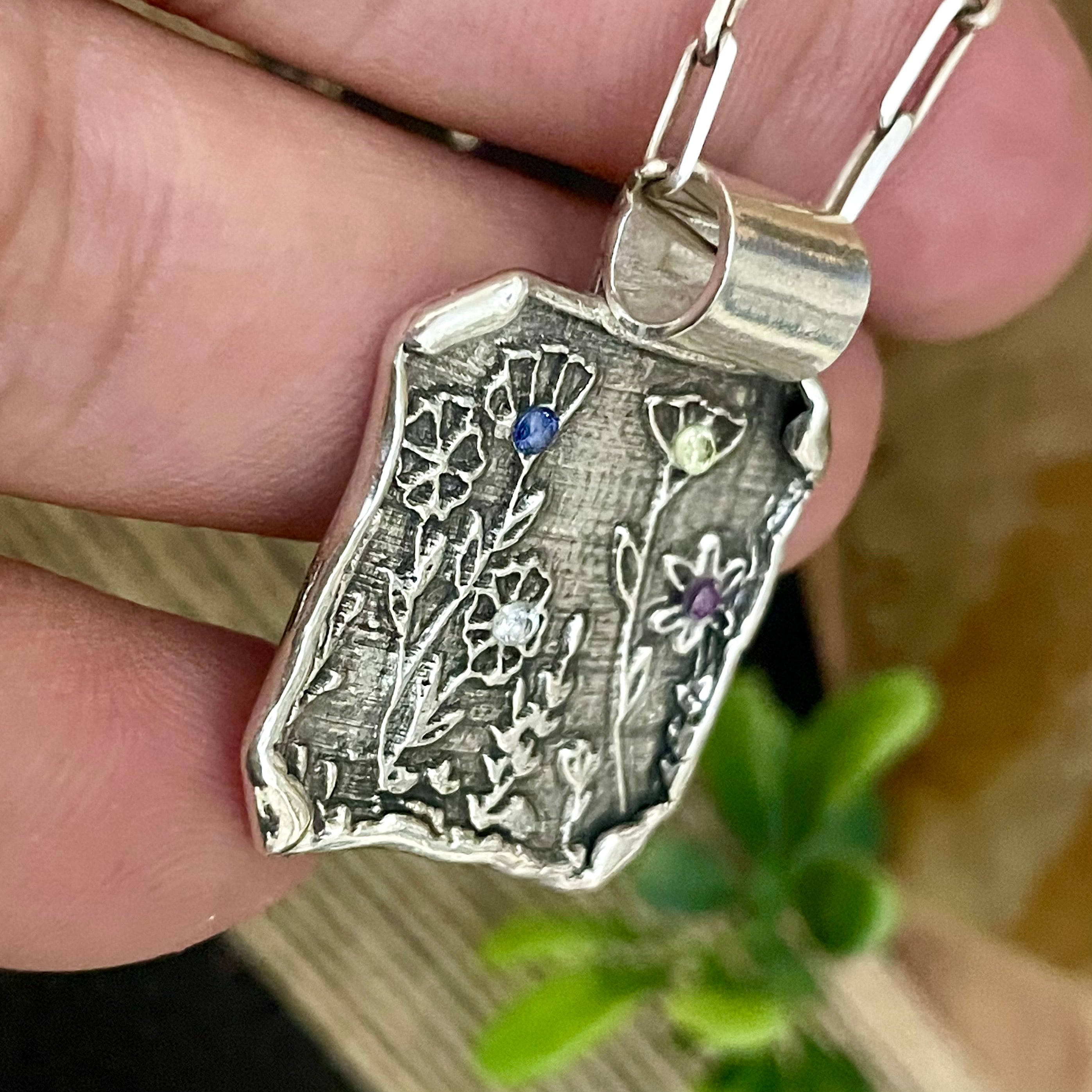 Silver pendant with floral designs and gemstones held by a hand
