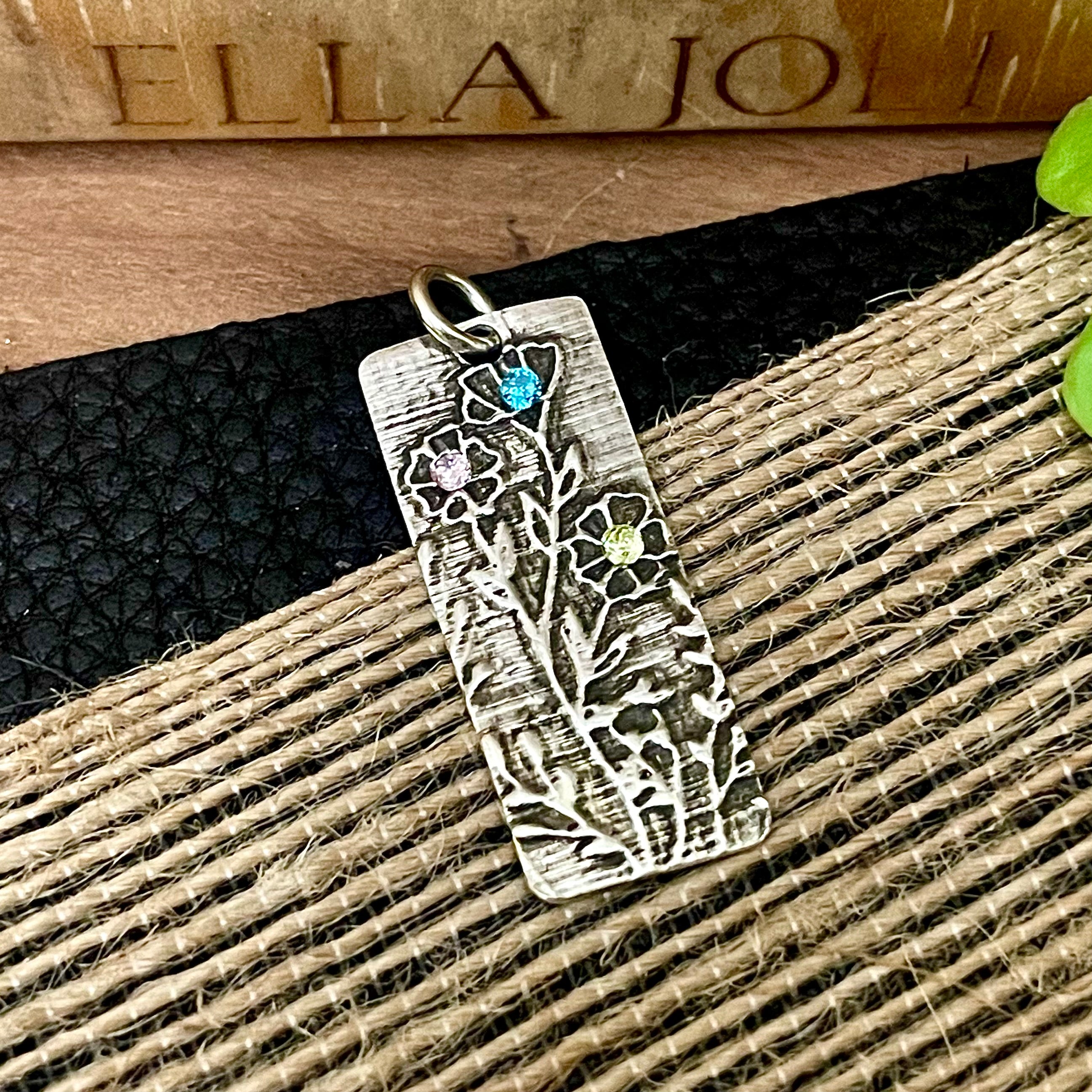 Silver pendant with floral design and gemstones on a textured surface