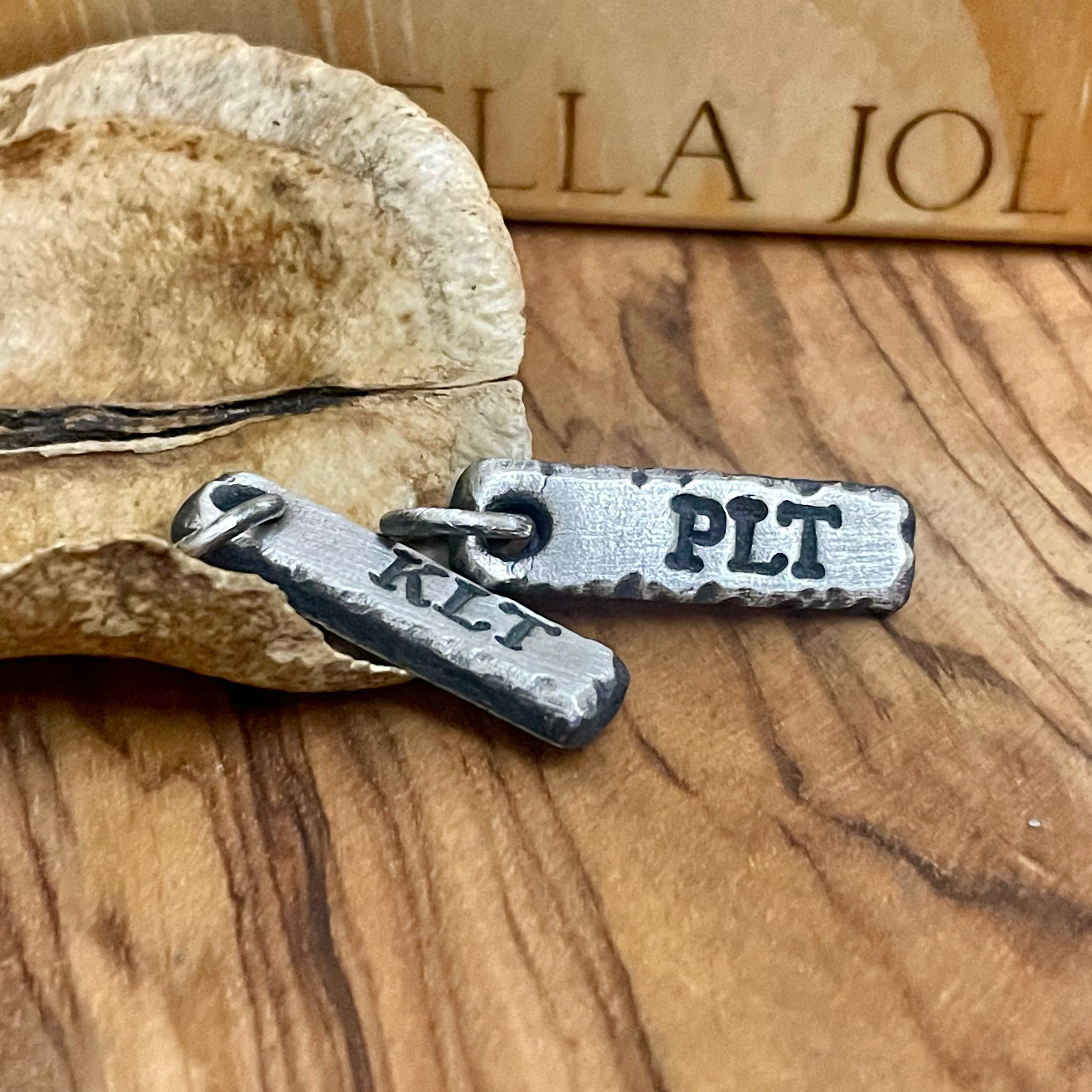 Two silver pendants with engraved text on a wooden surface.