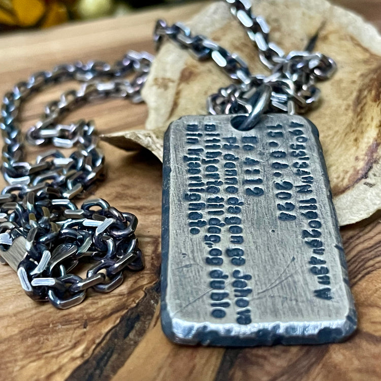 large oxidized sterling silver pendant with rustic engraved custom text hanging from thick sterling silver cable chain. Displayed on wood background