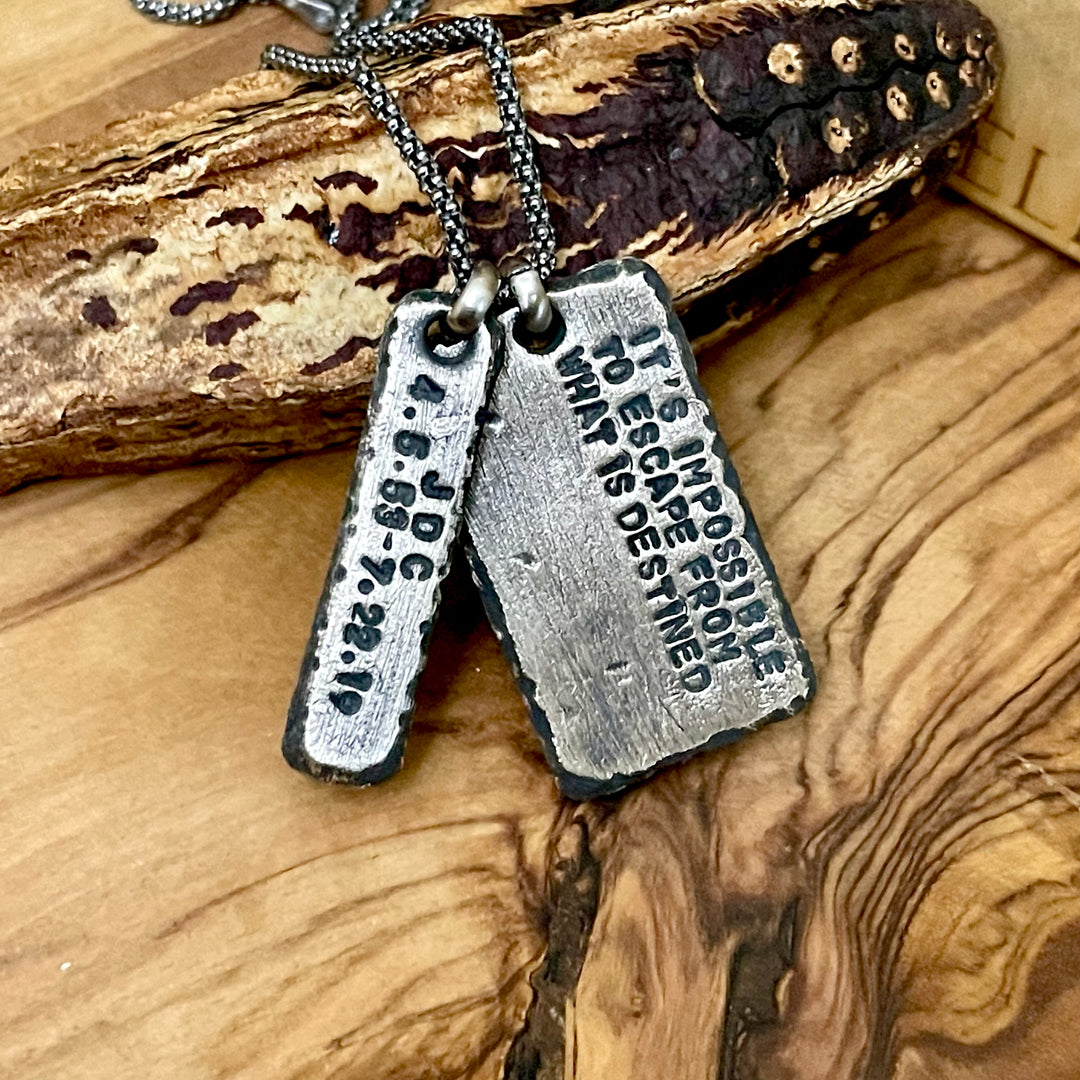 Two oxidized sterling silver pendants hanging from 1.8mm popcorn style chain with wood background. Custom engraving reads It&