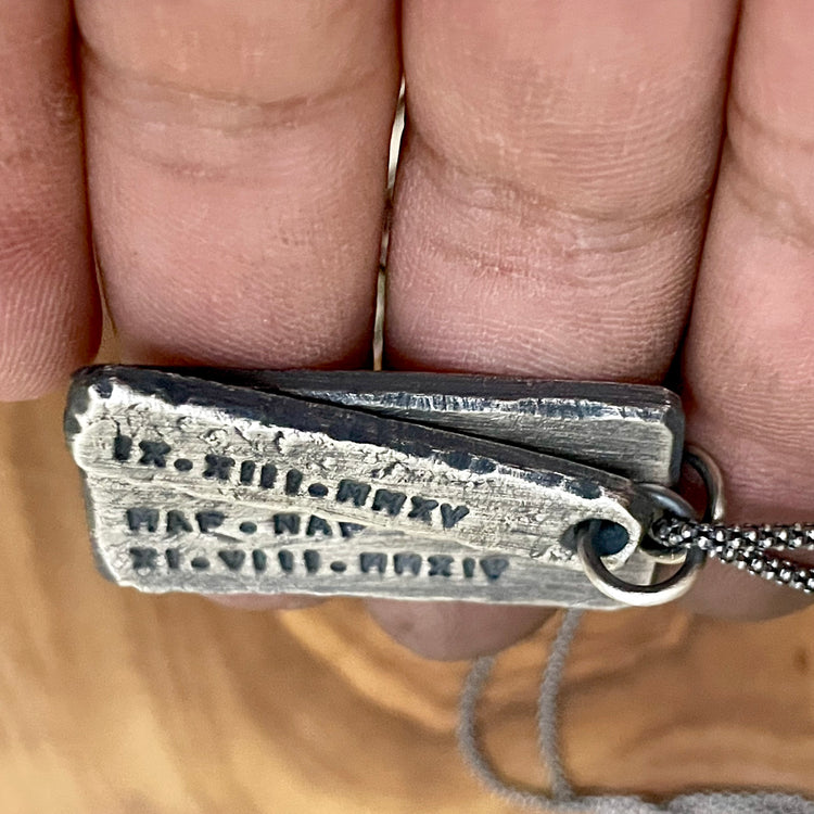 Side view of two personalized sterling silver rectangle shaped pendants hanging from sterling silver chain, laying in hand. 