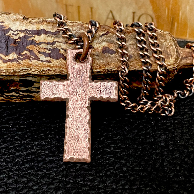 Pure copper cross pendant with pure copper curb chain on a textured surface. 