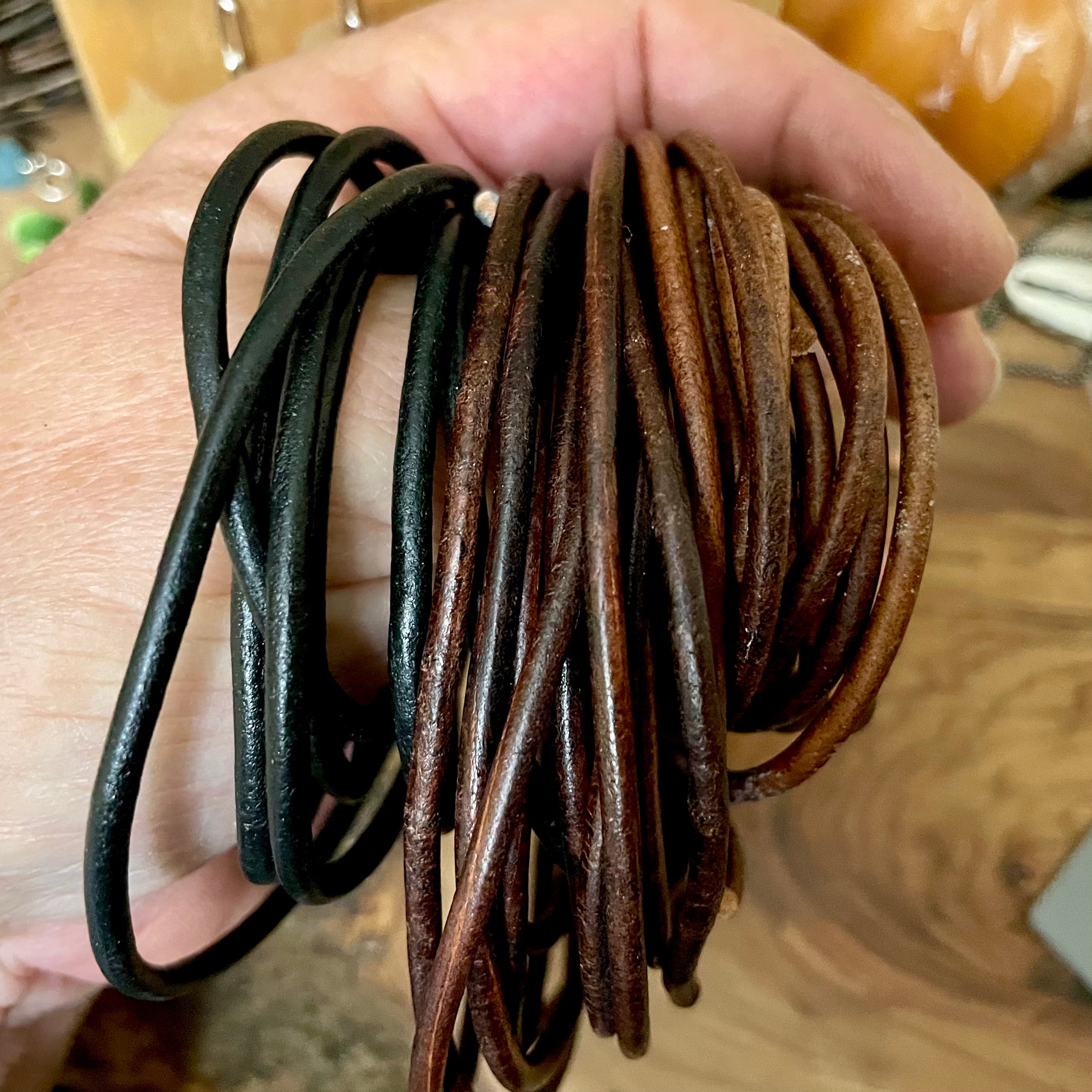 Hand holding black and brown leather necklaces on a wooden surface