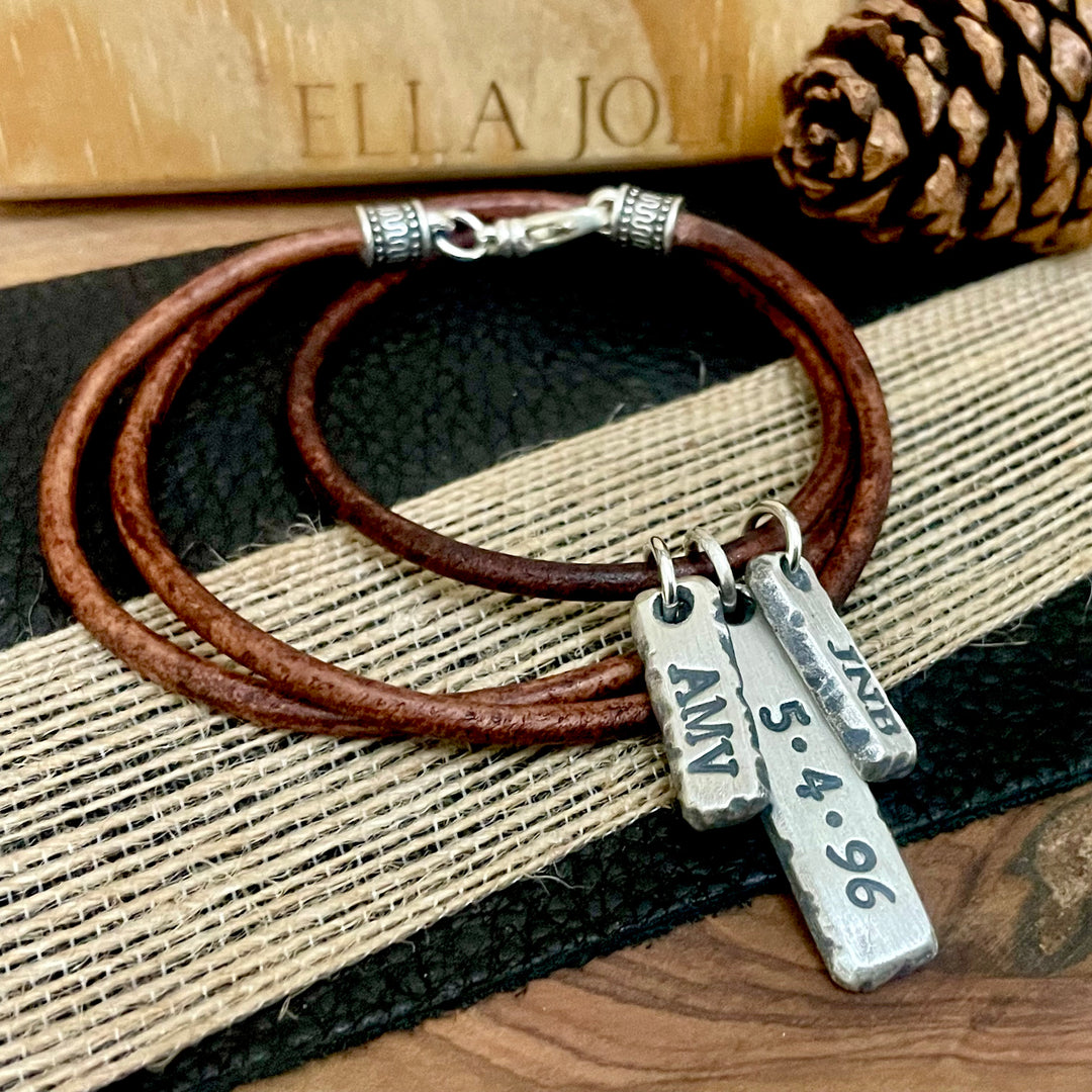 Brown leather necklace with sterling silver custom initial and date pendant and charms on a textured surface