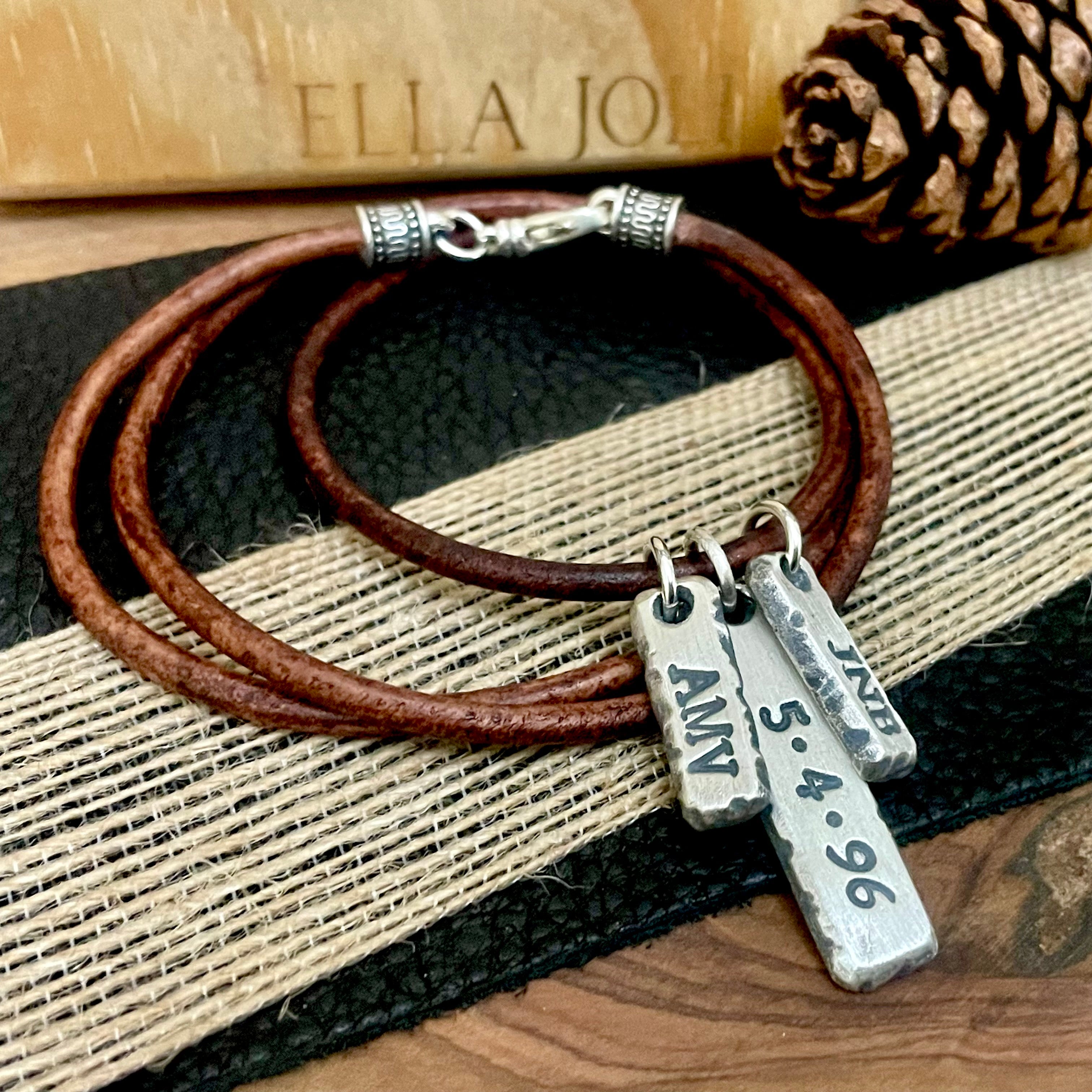Brown leather necklace with sterling silver custom initial and date pendant and charms on a textured surface