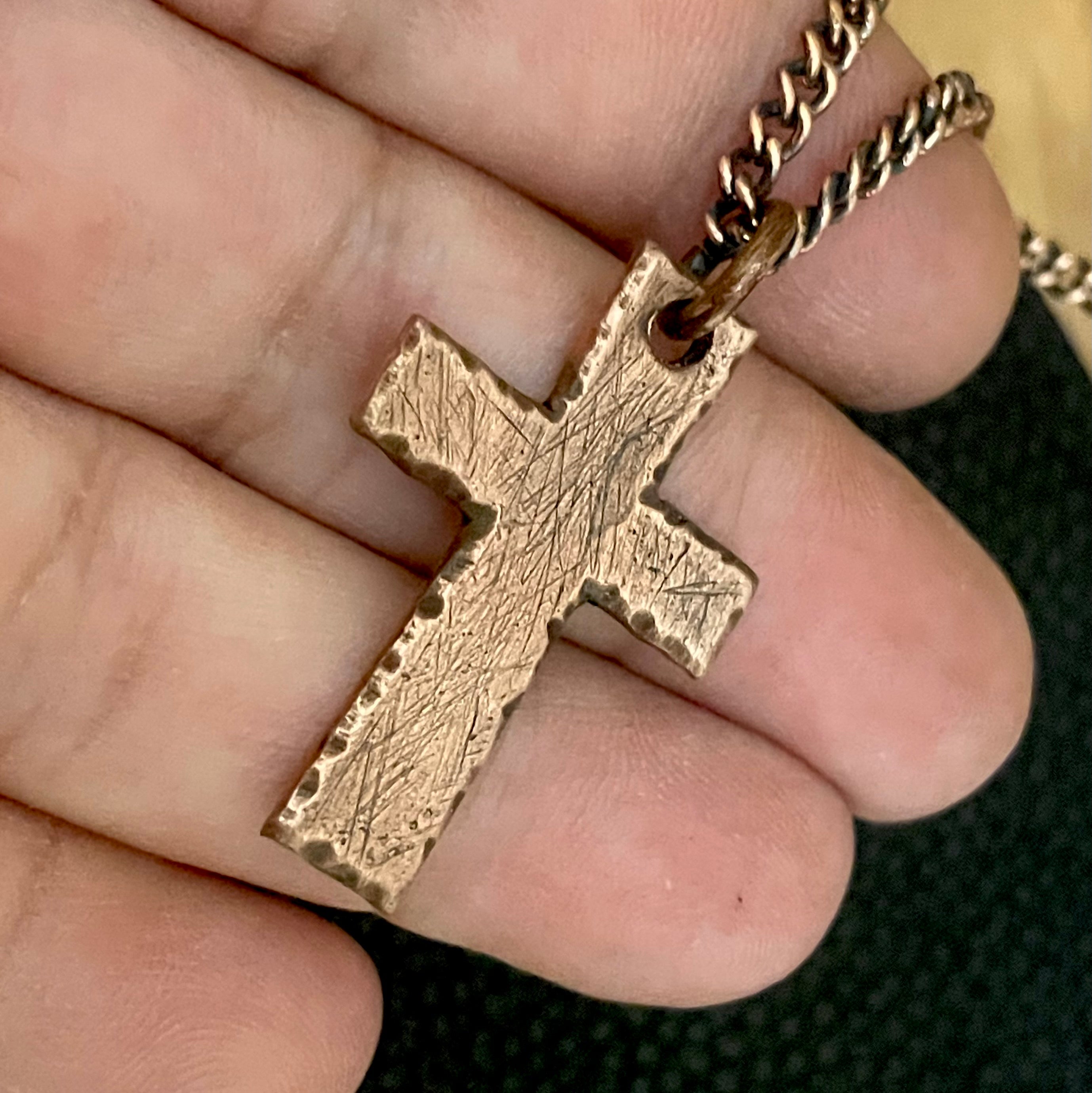 Antique solid copper cross pendant and chain held between fingers against a blurred background