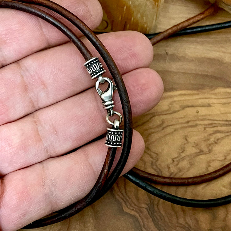 Brown leather cord with silver clasp held in a hand on a wooden surface