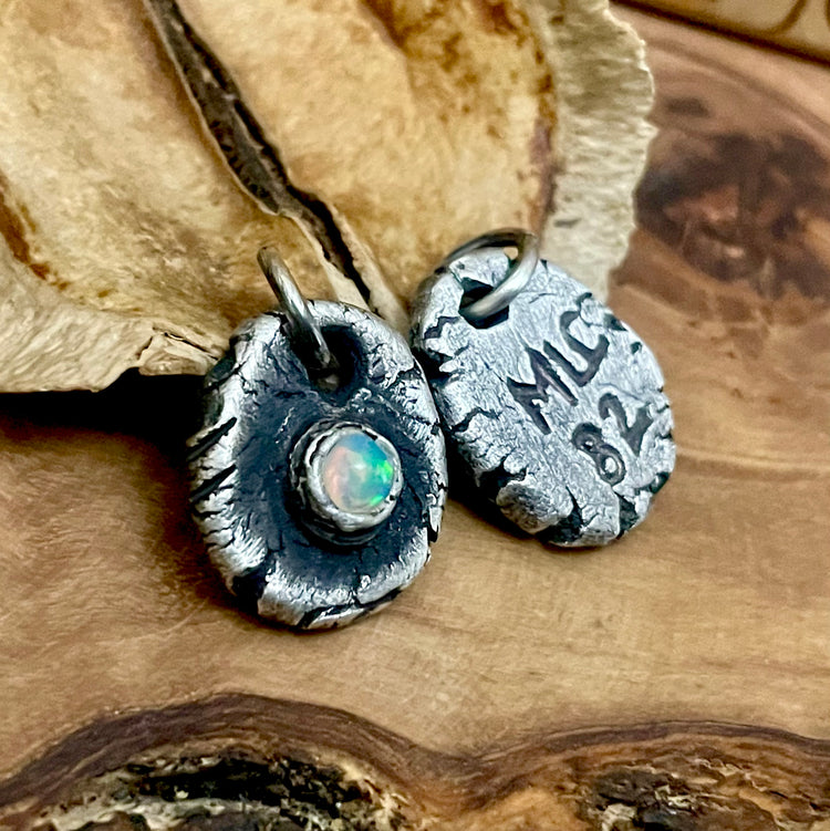 Pair of silver pendants with a central gemstone on a wooden surface