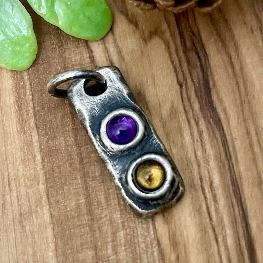 Silver pendant with purple and gold stones on a wooden surface