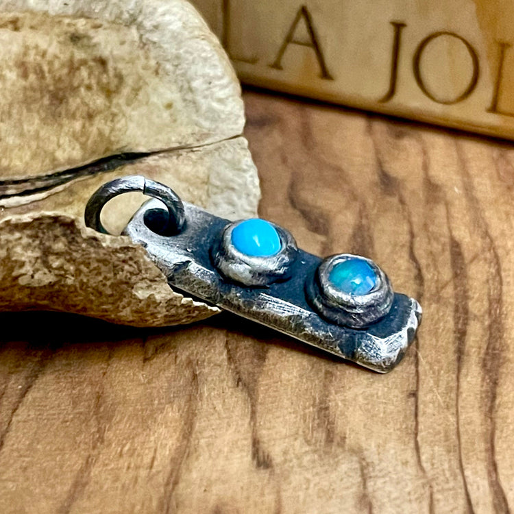 antique silver birthstone bar pendant with two blue gemstones on wood surface
