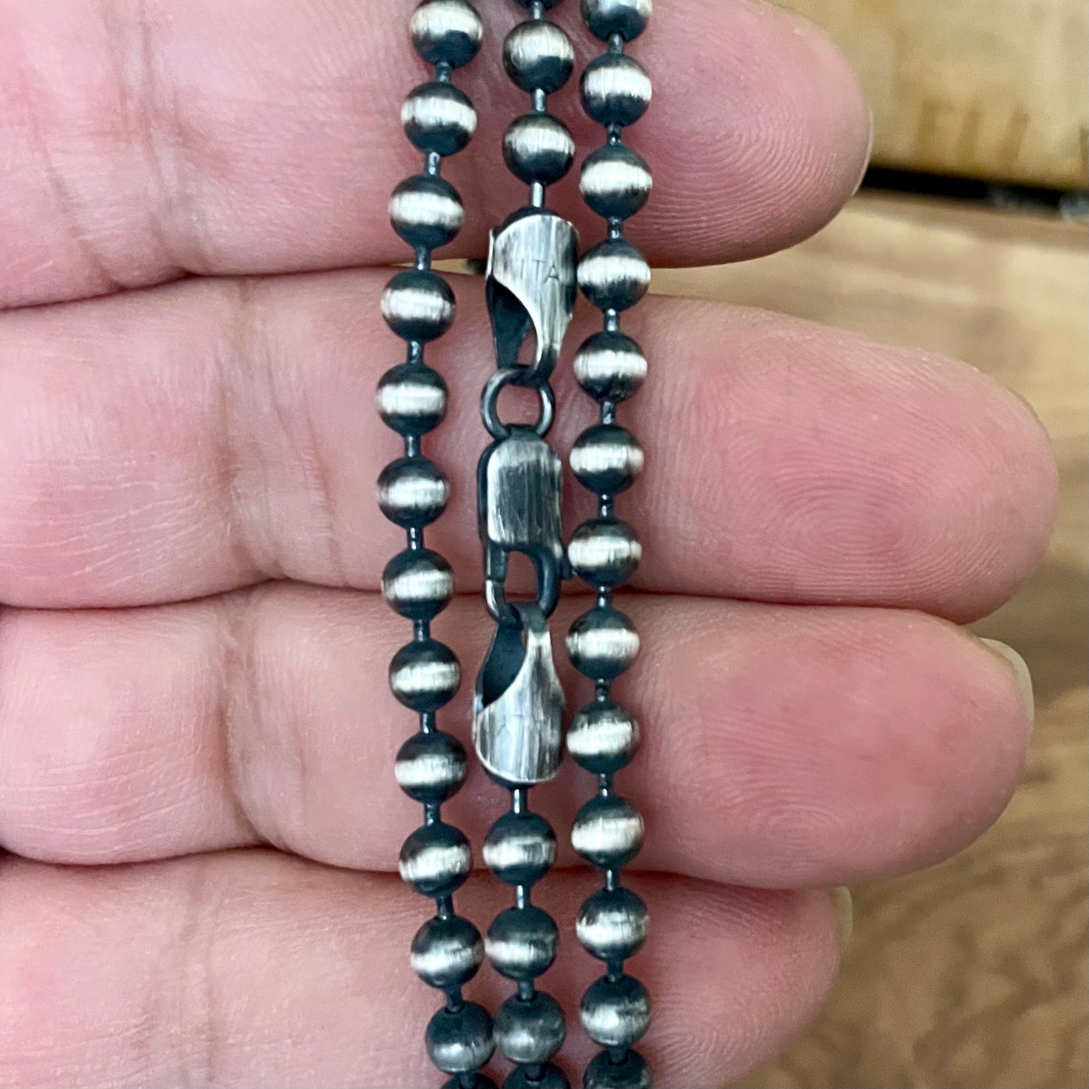 925 Sterling Silver beaded ball chain necklace held between fingers with a blurred background