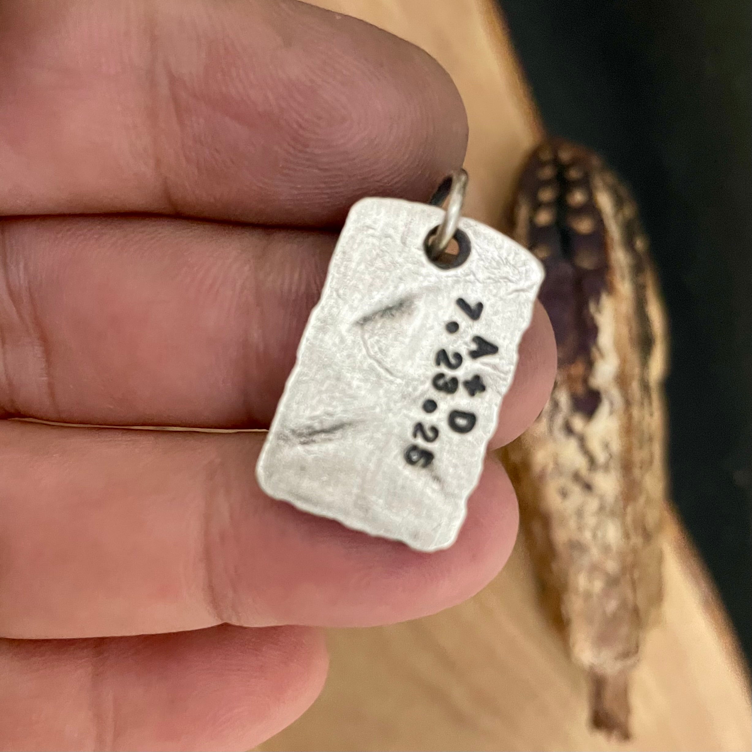 Back side of silver pendant with engraved text held between fingers