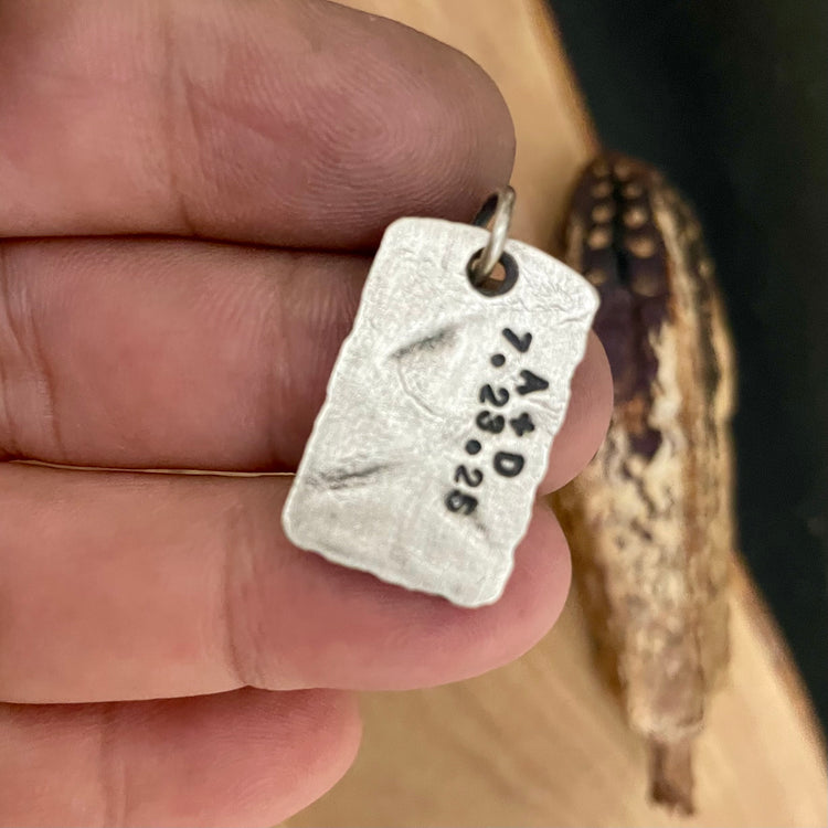 Back side of silver pendant with engraved text held between fingers