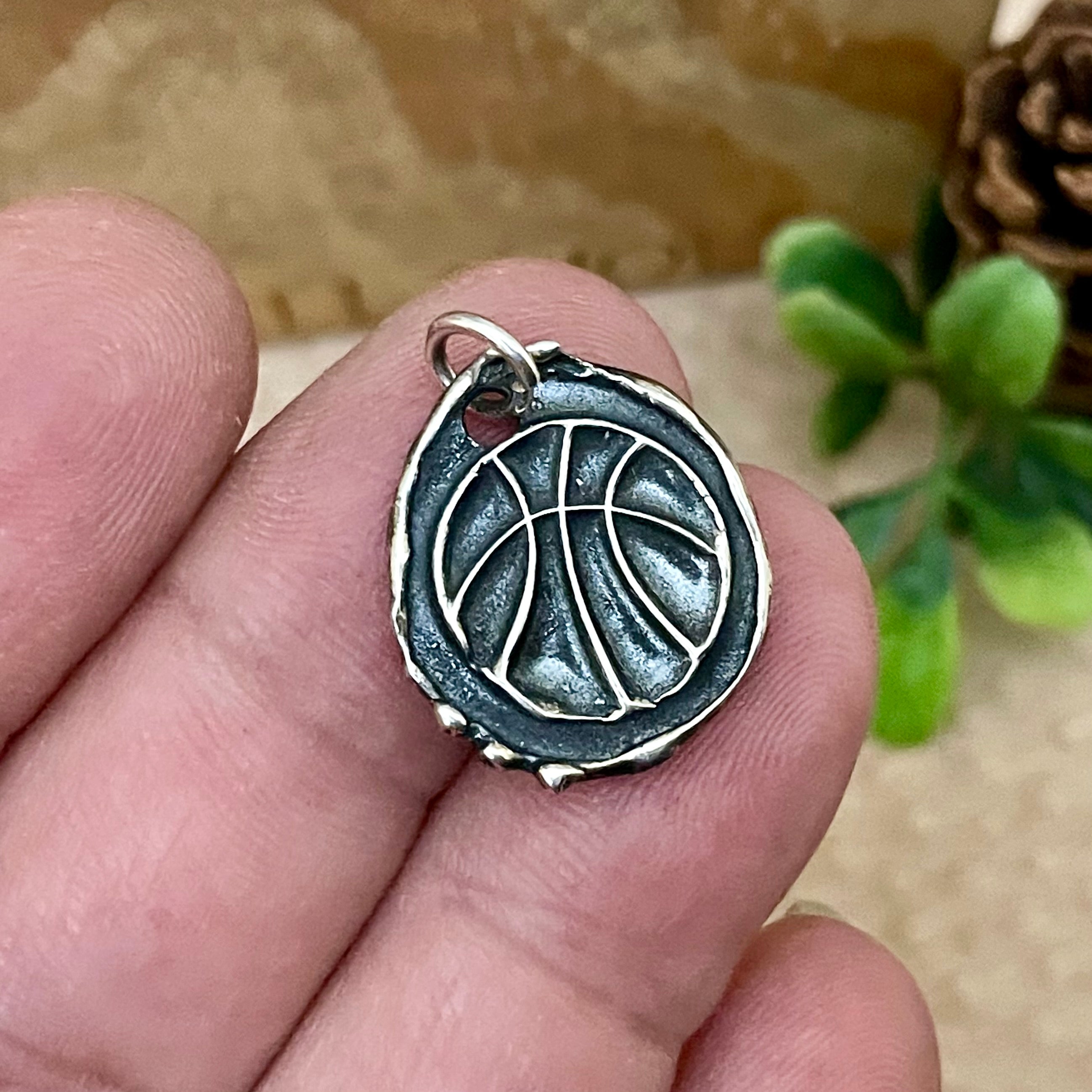 oxidized sterling silver basketball charm with raised artisan details. Can be personalized with name or number on backside. Displayed on fingers