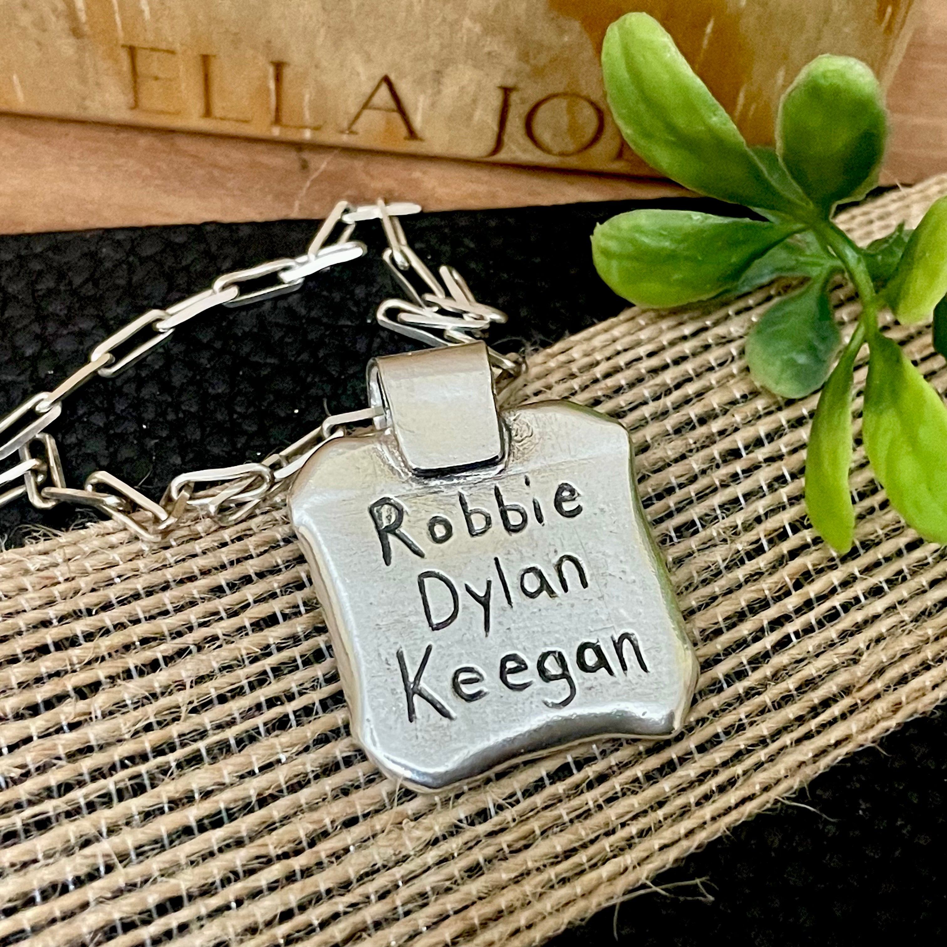 Silver back side of pendant with hand engraved names on a textured surface with a plant