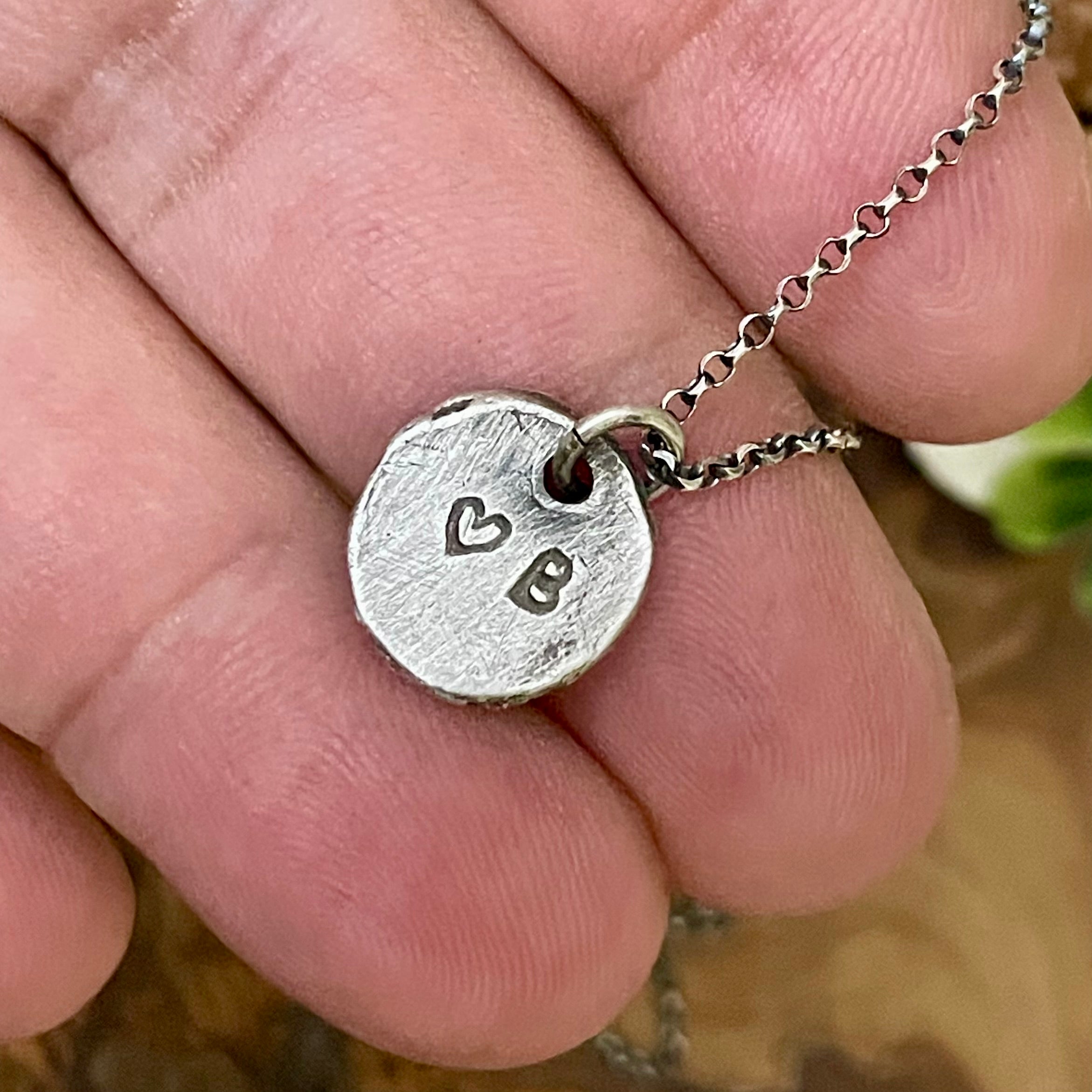 Silver necklace with a heart and 'B' pendant held between fingers.