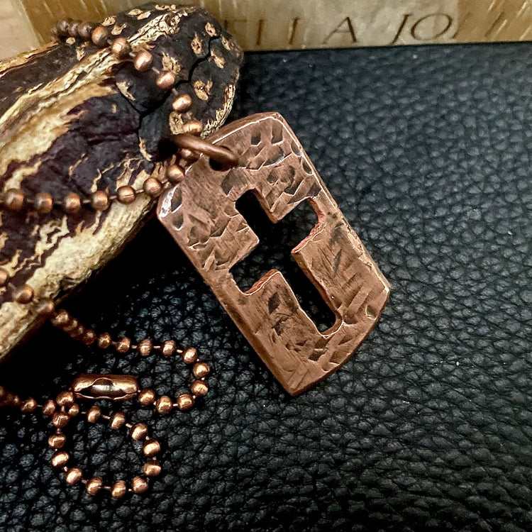 Copper cross pendant and chain on a textured black surface